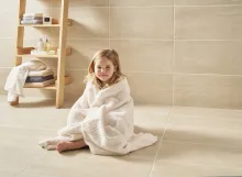 Little girl sat wrapped cosily in a towel on the bathroom floor smiling
