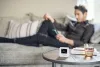 A man lounges on a sofa while a Wiser smart thermostat rests on a side table keeping the temperature comfortable